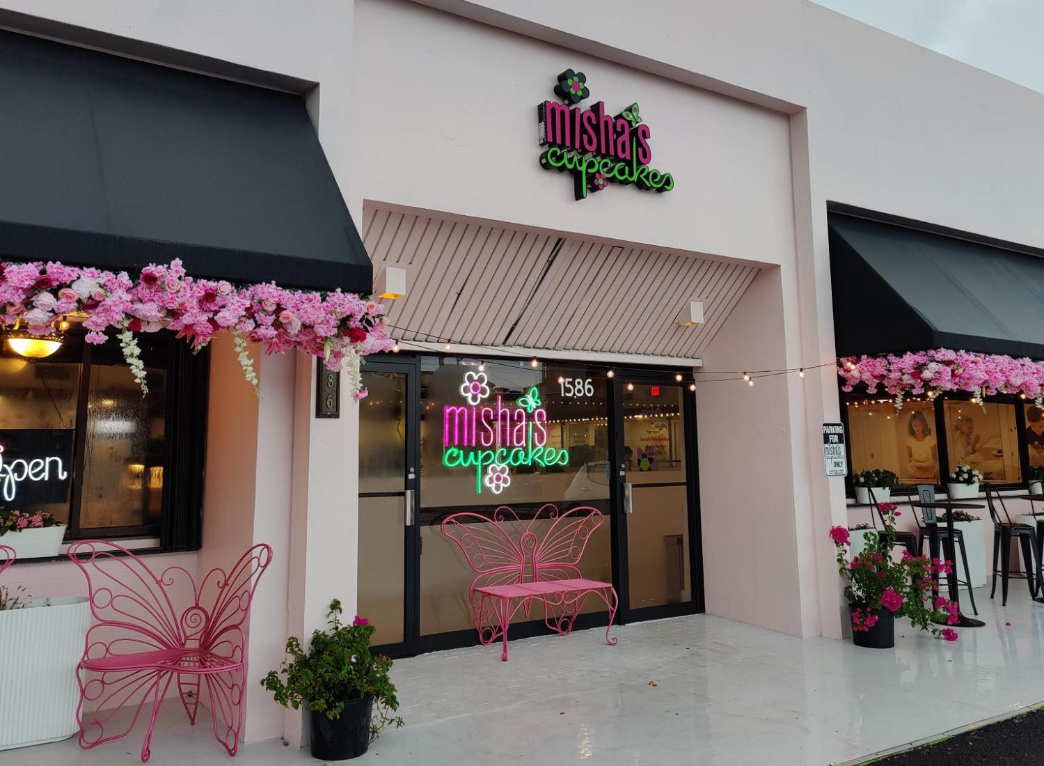 Pink storefront for Misha’s Cupcakes with floral decorations and outdoor seating.