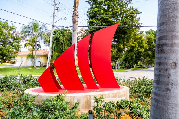 Red sculpture stands on platform in the middle of grass and shrubs