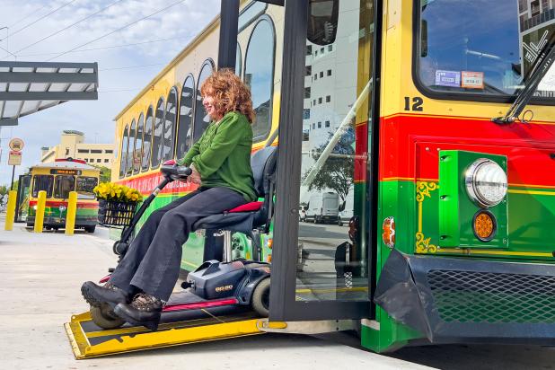 On sunny day with clouds, a woman with a green shirt sits on her wheelchair on the trolley's ramp
