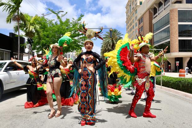 Street parade with dancers in colorful costumes and feathered headdresses performing energetically in downtown Coral Gables on sunny day
