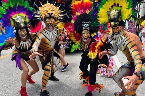 Performers in vibrant animal-themed costumes with feathered headdresses and tiger face paint pose energetically during the Carnaval de Barranquilla parade in Coral Gables