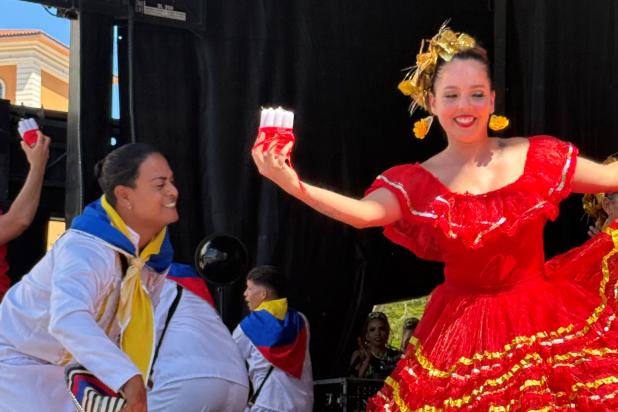 Woman in red, traditional Colombian dress dances with men in white outfits with Colombian colored scarves. 