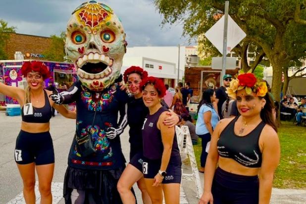Women in flower crowns pose next to person in huge skeleton day of the dead mascot costume