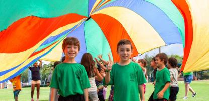 Kids playing in a field under a colorful parachute