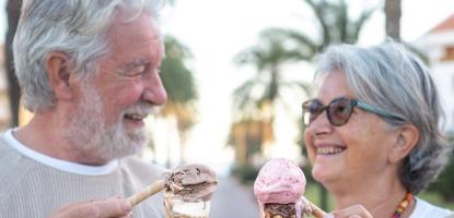 Two grey hair adults smile at each other holding dripping ice cream cones