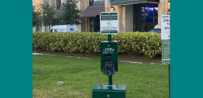 A dark green case with dog waste bags attached above a trash can
