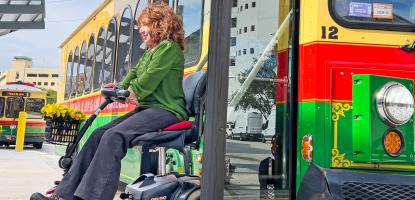 On sunny day with clouds, a woman with a green shirt sits on her wheelchair on the trolley's ramp