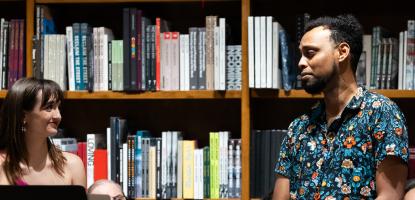 Woman and man look at each other with stands holding their readings and books are behind them