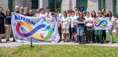 Employees hold up the Autism Flag on a sunny day in the back of City Hall area