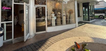 Storefront with white windows. Part of it is in the shade and the rest is lit by a warm sunlight. In the background a shining blue sky with clouds