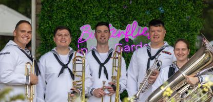 Unfocused foreground of flowers and Navy Brass Quartet in white uniform with instruments focused in the background