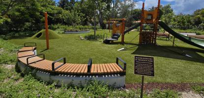 Playground at Mayor Dorothy Thomson Park featuring slides, climbing structures, benches, and shaded seating surrounded by greenery under a bright sky. [PDF]