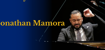 Jonathan Mamora in suit, one hand raised, playing the piano in a dark background
