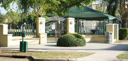 Entrance to Phillips Park with sidewalks and green closed gate on a sunny day
