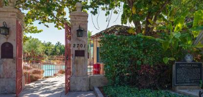 Entrance to the Venetian Pool in Coral Gables showing two stone pillars with open red iron gates leading to the turquoise pool beyond.