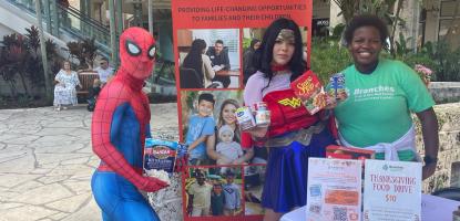 Spiderman and Wonder Woman and woman in green Branches organization tshirt pose in front of plaza behind booth