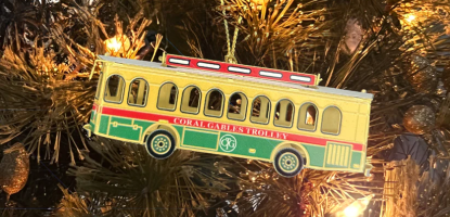 Yellow, red, and green Coral Gables trolley as an ornament hanging on a tree with white lights