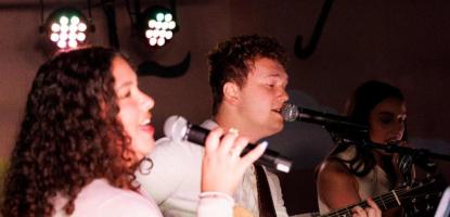 Woman and a man with a guitar sitting down sing into their mics