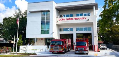 White, modern Fire House 4 with two red fire trucks in the driveway with blue sky in the background