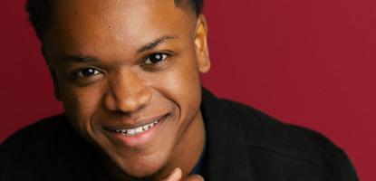 Langston Hughes II smiling wearing black with a red background