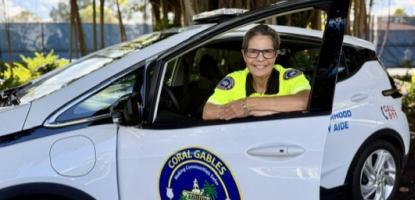 Woman in NSA uniform stands behind car door smiling with large tree and sunlight in the background