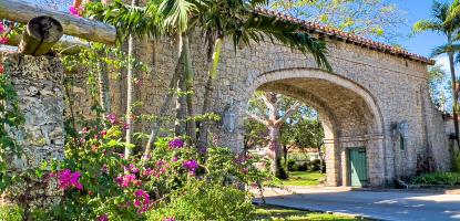 Pink flowers and palm trees cover the rock entrance on clear sunny day