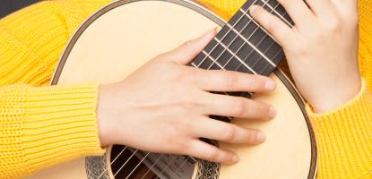 Guitarist Leonela Alejandro smiles while holding a classical guitar and wearing a yellow sweater.