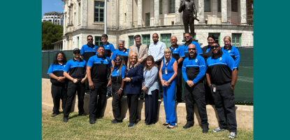 Code Enforcement Officers and staff in blue pose in front of City Hall, sunny day blue sky
