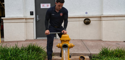 A Coral Gables firefighter tests a yellow fire hydrant as water flows from the open outlet outside a fire station.