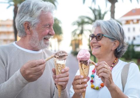 Two grey hair adults smile at each other holding dripping ice cream cones