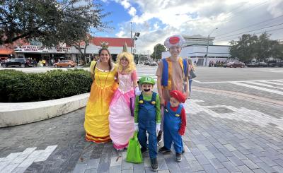 On sunny day, People stand on Miracle Mile dressed as Daisy, Princess Peach, Luigi, Mario, and Toad