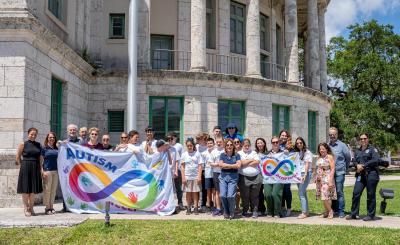 Employees hold up the Autism Flag on a sunny day in the back of City Hall area
