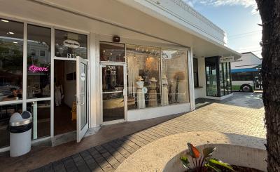 Storefront with white windows. Part of it is in the shade and the rest is lit by a warm sunlight. In the background a shining blue sky with clouds