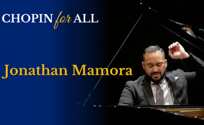 Jonathan Mamora in suit, one hand raised, playing the piano in a dark background