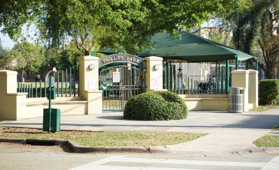 Entrance to Phillips Park with sidewalks and green closed gate on a sunny day