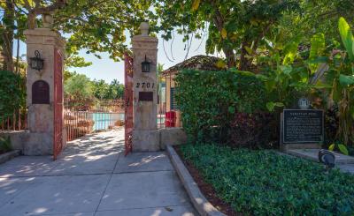 Entrance to the Venetian Pool in Coral Gables showing two stone pillars with open red iron gates leading to the turquoise pool beyond.