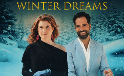 Woman in black and man in light blue suit smile in front of a snowy wonderland backdrop