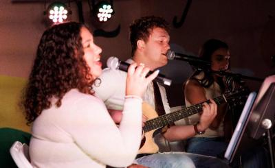 Woman and a man with a guitar sitting down sing into their mics