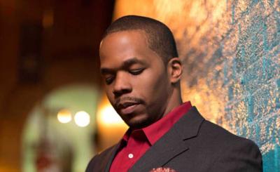 Warren Wolf wearing a suit with red shirt standing a lit alley
