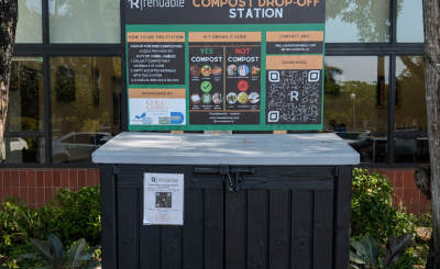 Wide compost bin on stone patch on mulch with sign that explains compost rules
