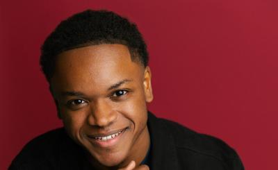 Langston Hughes II smiling wearing black with a red background