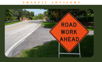Orange Road work ahead sign next to a road on sunny day