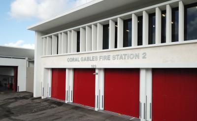 Large white building with four large, red garage doors and cloudy blue sky in the background