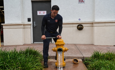 A Coral Gables firefighter tests a yellow fire hydrant as water flows from the open outlet outside a fire station.