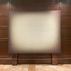 Large abstract painting with a light center fading to darker edges, displayed against a wooden wall.