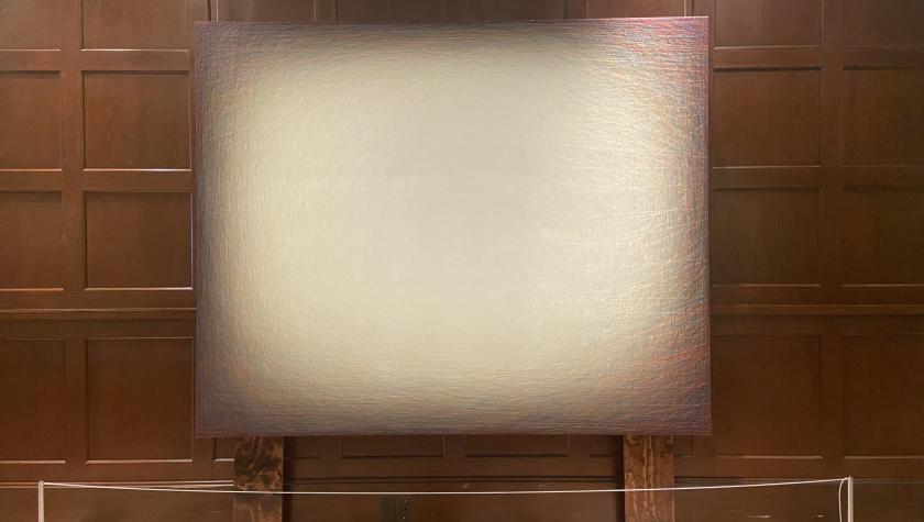 Large abstract painting with a light center fading to darker edges, displayed against a wooden wall.